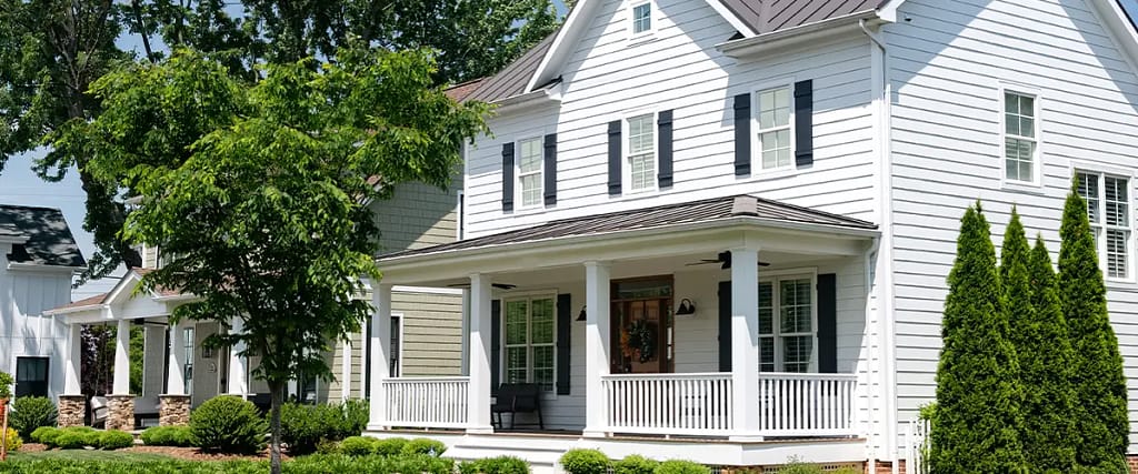 Modern white siding home with black shutters and front porch in a suburban neighborhood with manicured landscaping