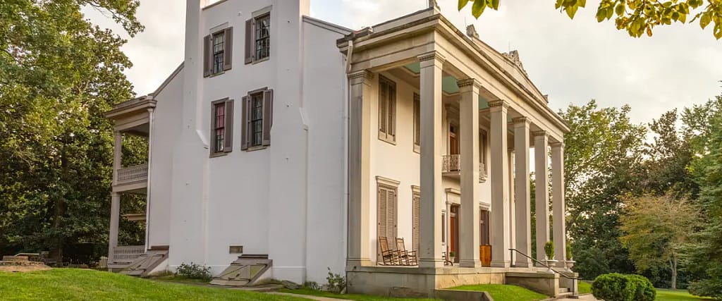 Large historic Southern home with tall white columns and red brick accents surrounded by trees and green lawn